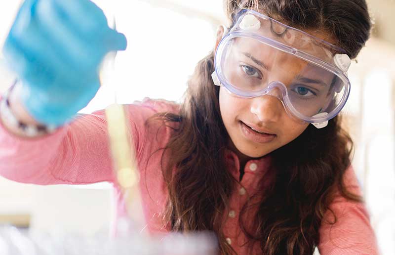 Girl in safety goggles and gloves filling test tube Girl in safety goggles and gloves filling test tube