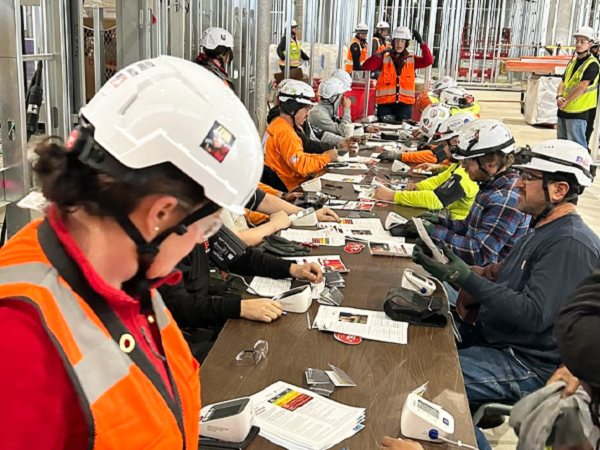 Four people in hard hats holding up red American Heart Association shirts.