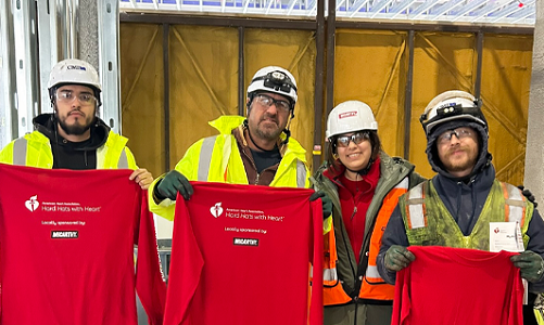 Four people in hard hats holding up red American Heart Association shirts.