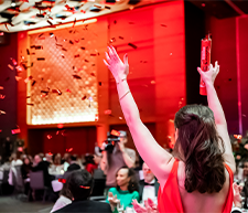 Photo of a woman standing with her back to the camera with her hands in the air and confetti falling from the ceiling.